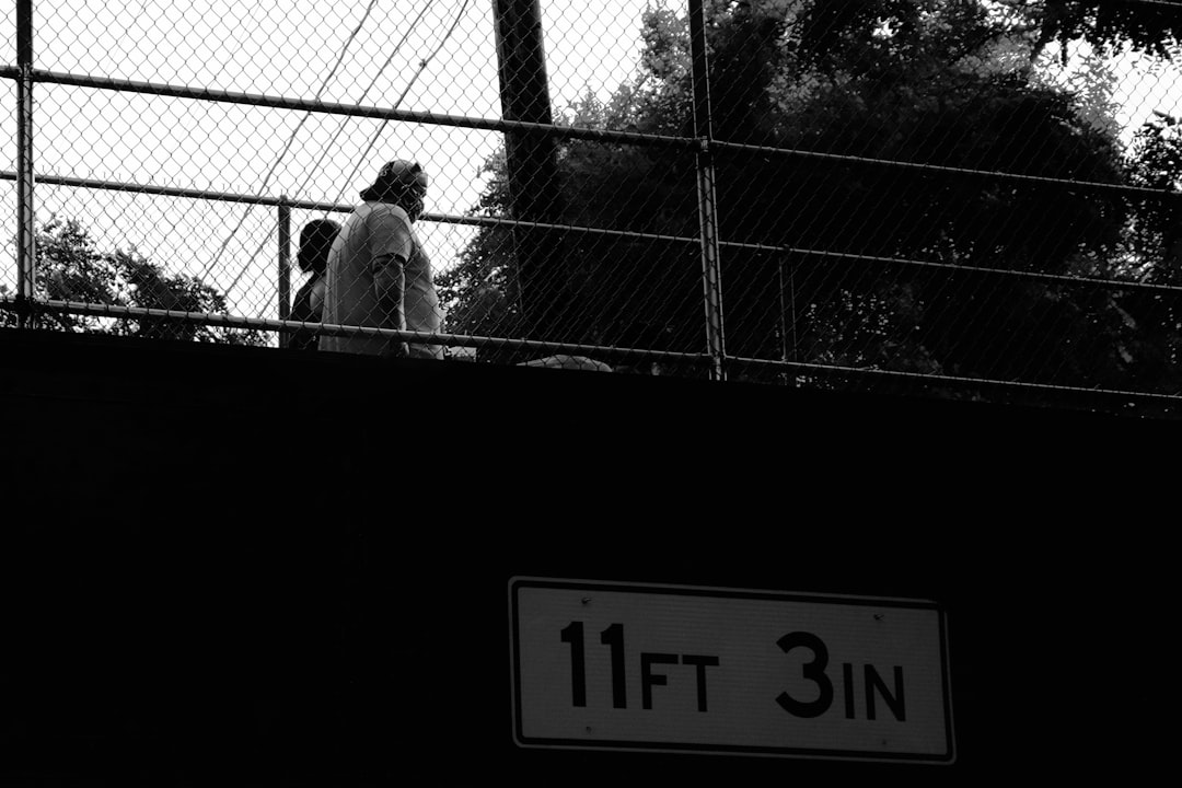 grayscale photo of man standing beside fence