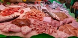 A seafood display at a market featuring a variety of fish and shellfish. The arrangement includes red shrimp, whole fish like sea bass, cuttlefish, and possibly flatfish. Ice is used as a base to keep the seafood fresh, and there are handwritten price tags indicating different prices for each item.