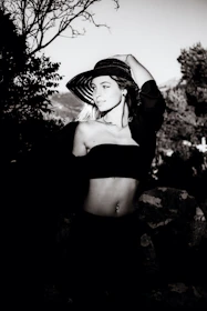 Giovana posing outdoors in a chic sun hat and flowing dress, capturing the essence of luxurious lifestyle.