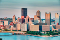 The downtown Pittsburgh skyline above a river on a clear evening