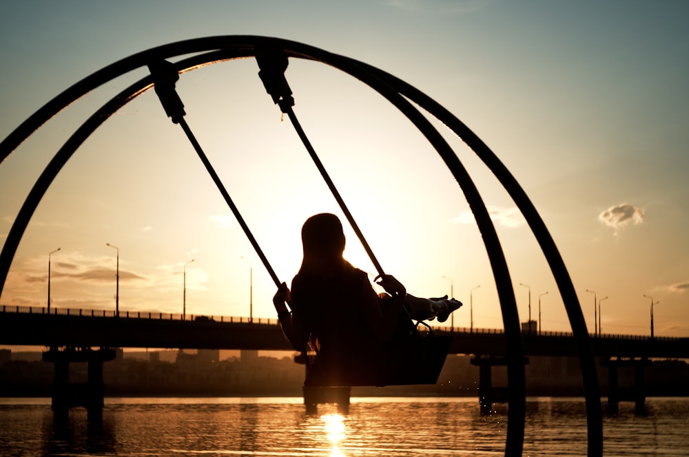 man in black jacket sitting on swing during sunset