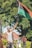 A man is holding up a Pan-African flag in an outdoor setting with trees in the background. He is wearing a grey tank top and a cap, while other individuals stand around, some wearing masks.