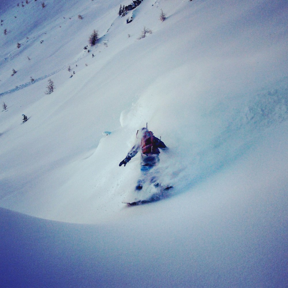 persona in giacca rossa e pantaloni neri sulla montagna coperta di neve durante il giorno