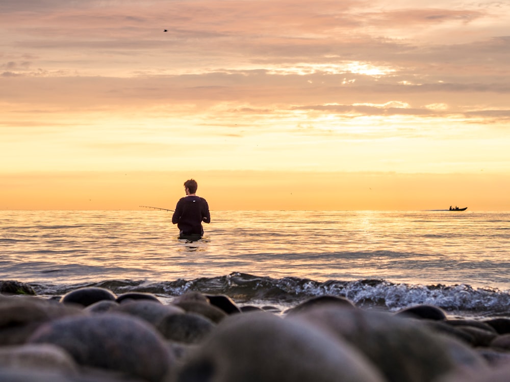 silhouette of man sitting on rocky shore during sunset