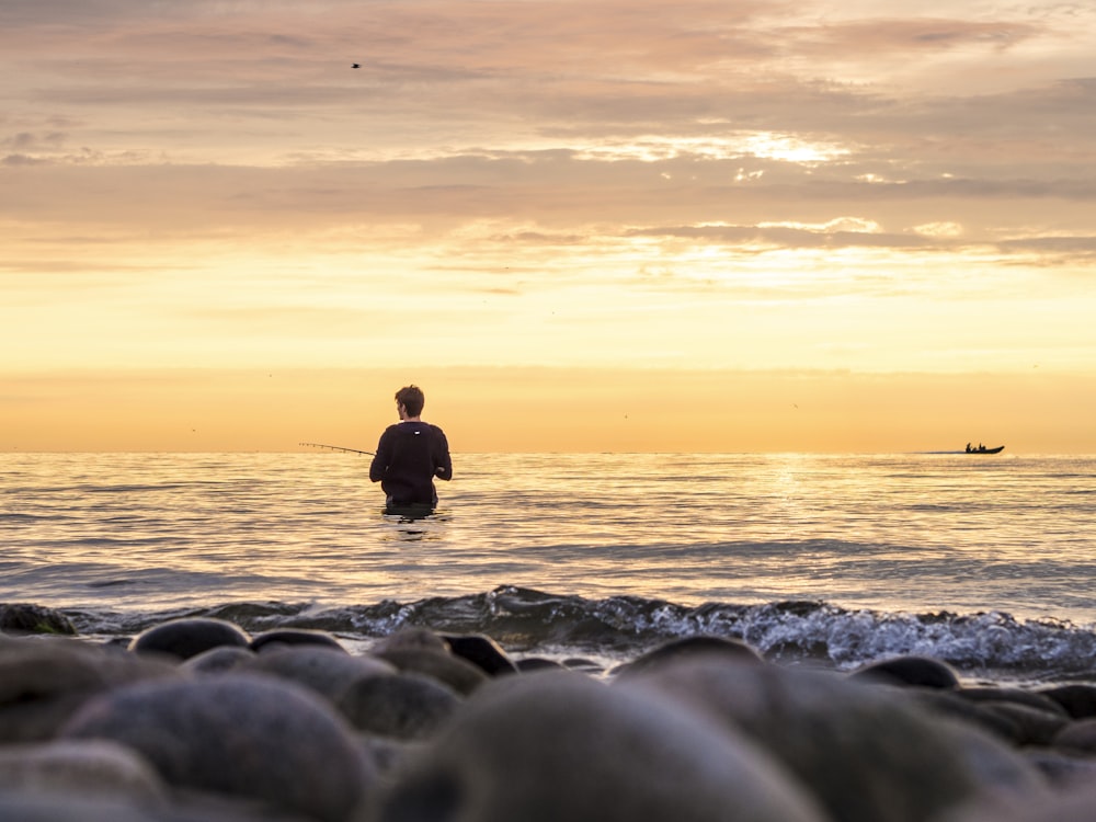 silhouette of man sitting on rocky shore during sunset