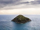 green and brown rock formation on blue sea under white clouds during daytime