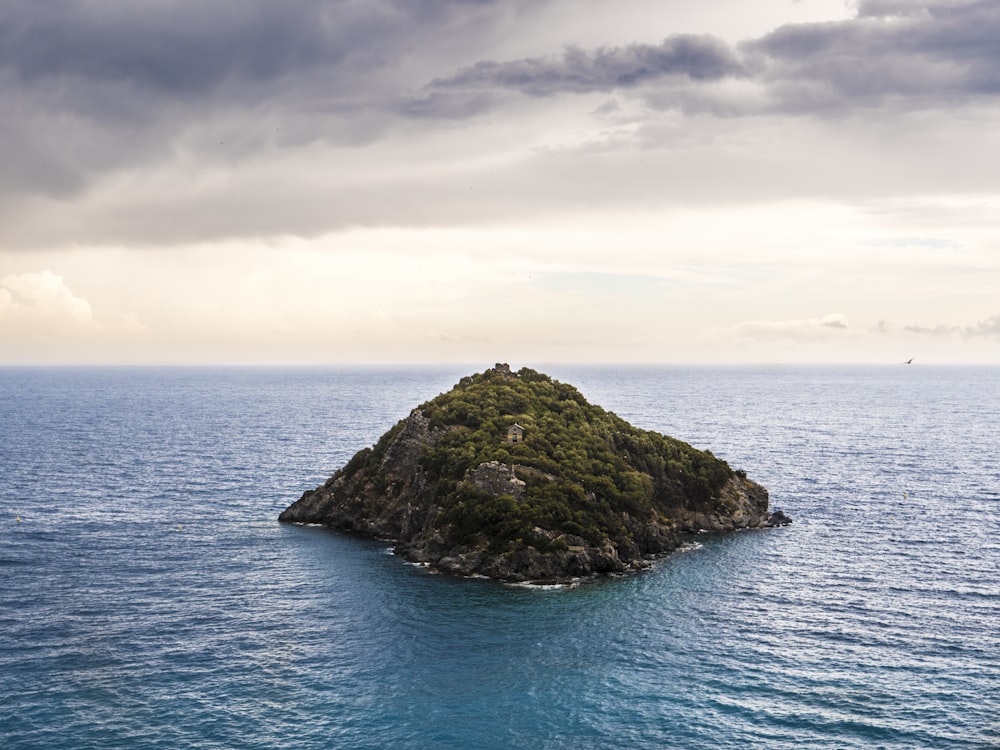 formação rochosa verde e marrom no mar azul sob nuvens brancas durante o dia