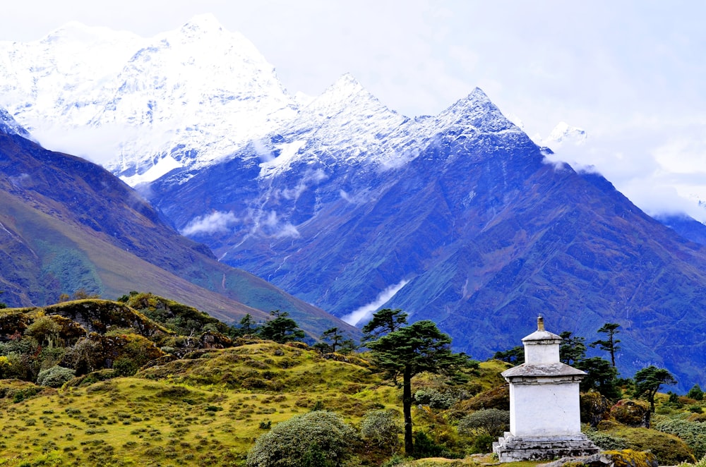 white concrete cross on green grass field near mountain under white clouds during daytime