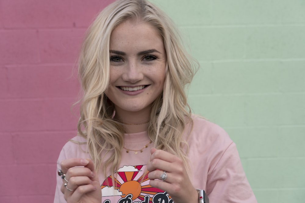 mulher sorridente na camisa rosa do pescoço da tripulação segurando o caso do iphone da impressão do coração vermelho e branco