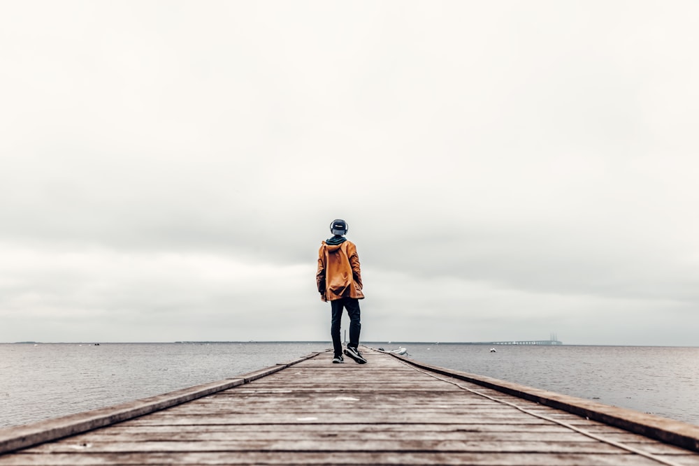 woman in orange jacket and black pants standing on wooden dock