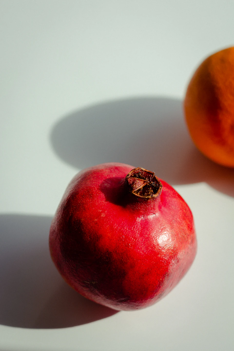 Close-up view of pomegranate and orange on white surface against gray background together