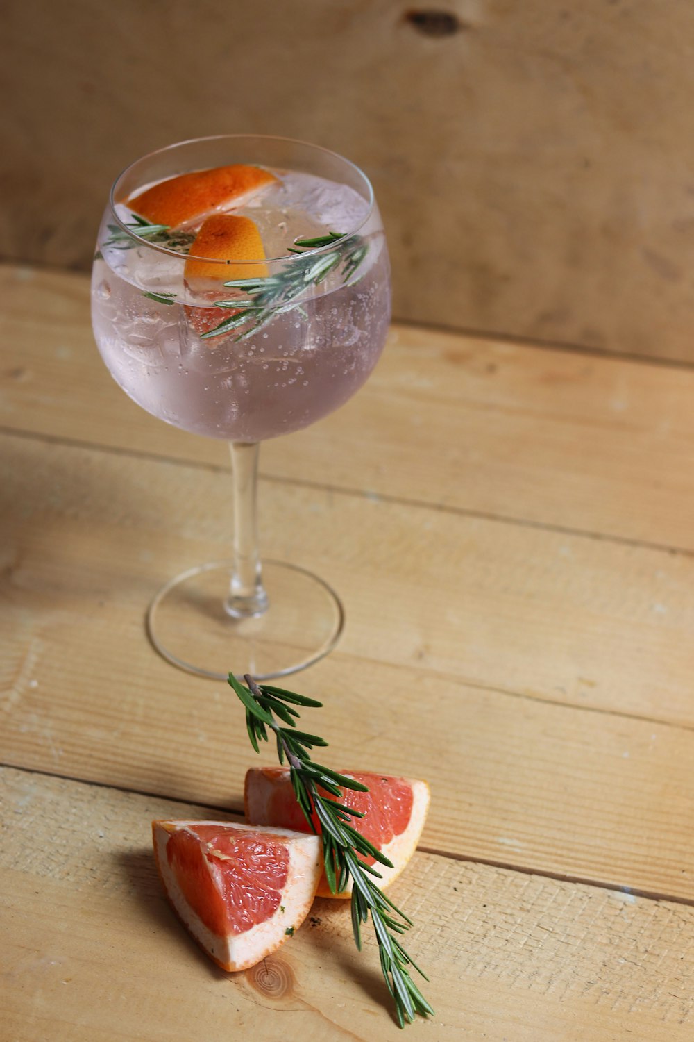 clear wine glass with pink liquid and sliced of strawberry on brown wooden table