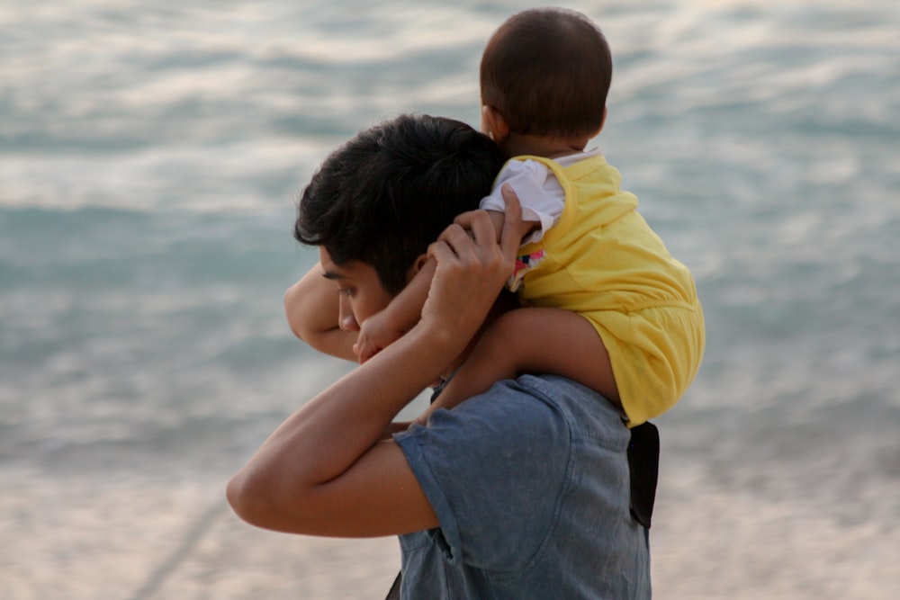 boy in yellow shirt kissing woman in blue denim jeans on beach during daytime