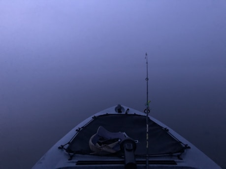 A stable kayak on calm blue ocean waters during sunrise, with a fisherman casting a line.