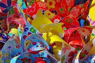 A colorful assortment of paper flowers with various vibrant patterns. The paper is folded and arranged to create an intricate and lively display. Floral designs in red, yellow, blue, and multicolored hues dominate the image, creating a cheerful and festive atmosphere.