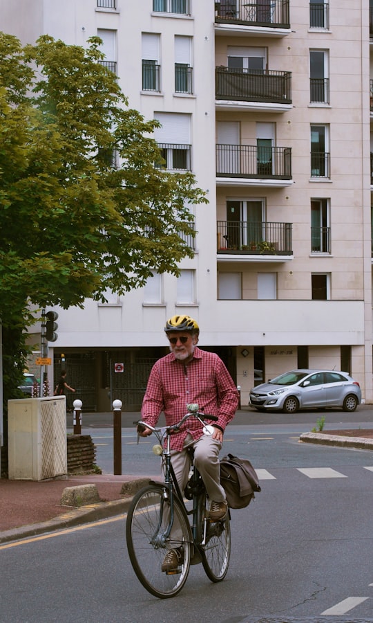 man in red dress shirt riding on bicycle during daytime in Créteil France