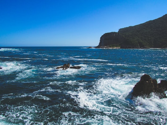 ocean waves crashing on rock formation under blue sky during daytime in Knysna South Africa
