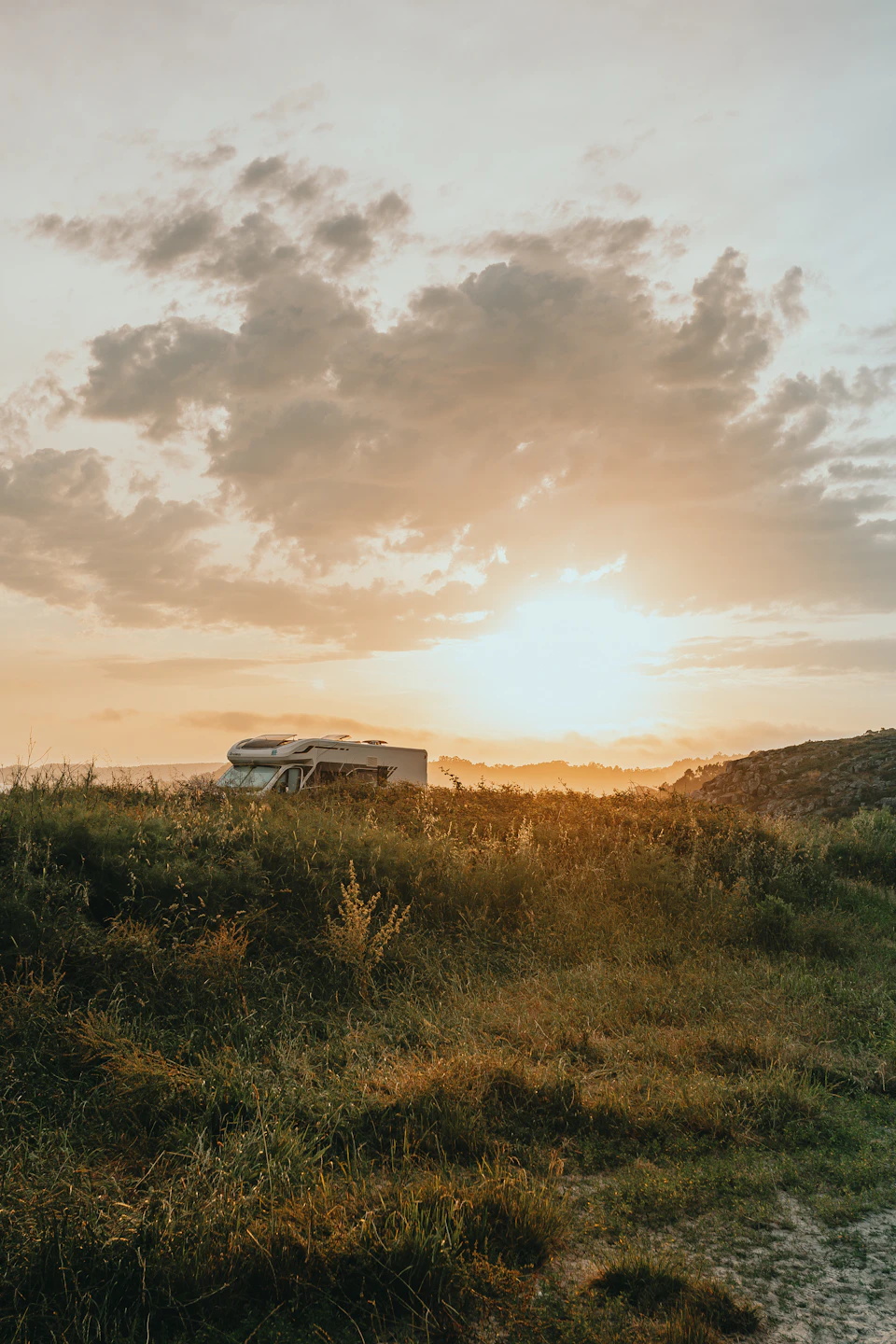 Serene landscape at sunset with white car parked on grassy hillside under warm sky colors