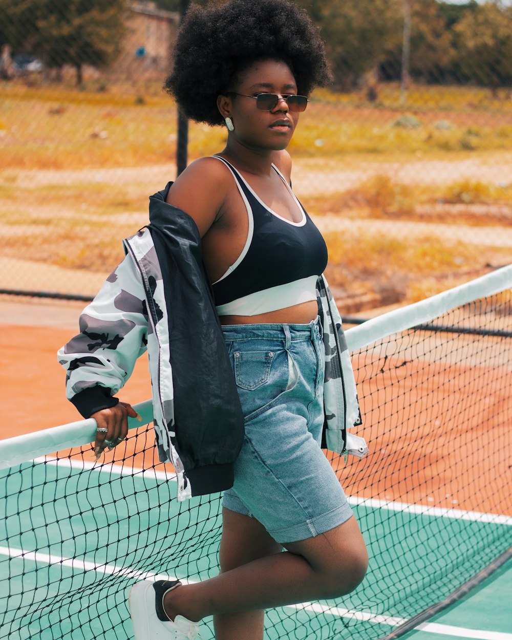 woman in blue denim jacket and blue denim shorts standing beside white net during daytime