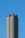 Three tall, cylindrical cement silos stand against a clear blue sky. The structures are slightly weathered, with darker top sections.