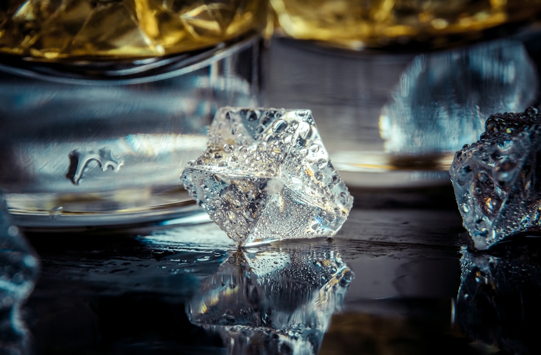 Selective focus pure whisky with ice cube inside whisky glass on wet background alcohol drink concept
