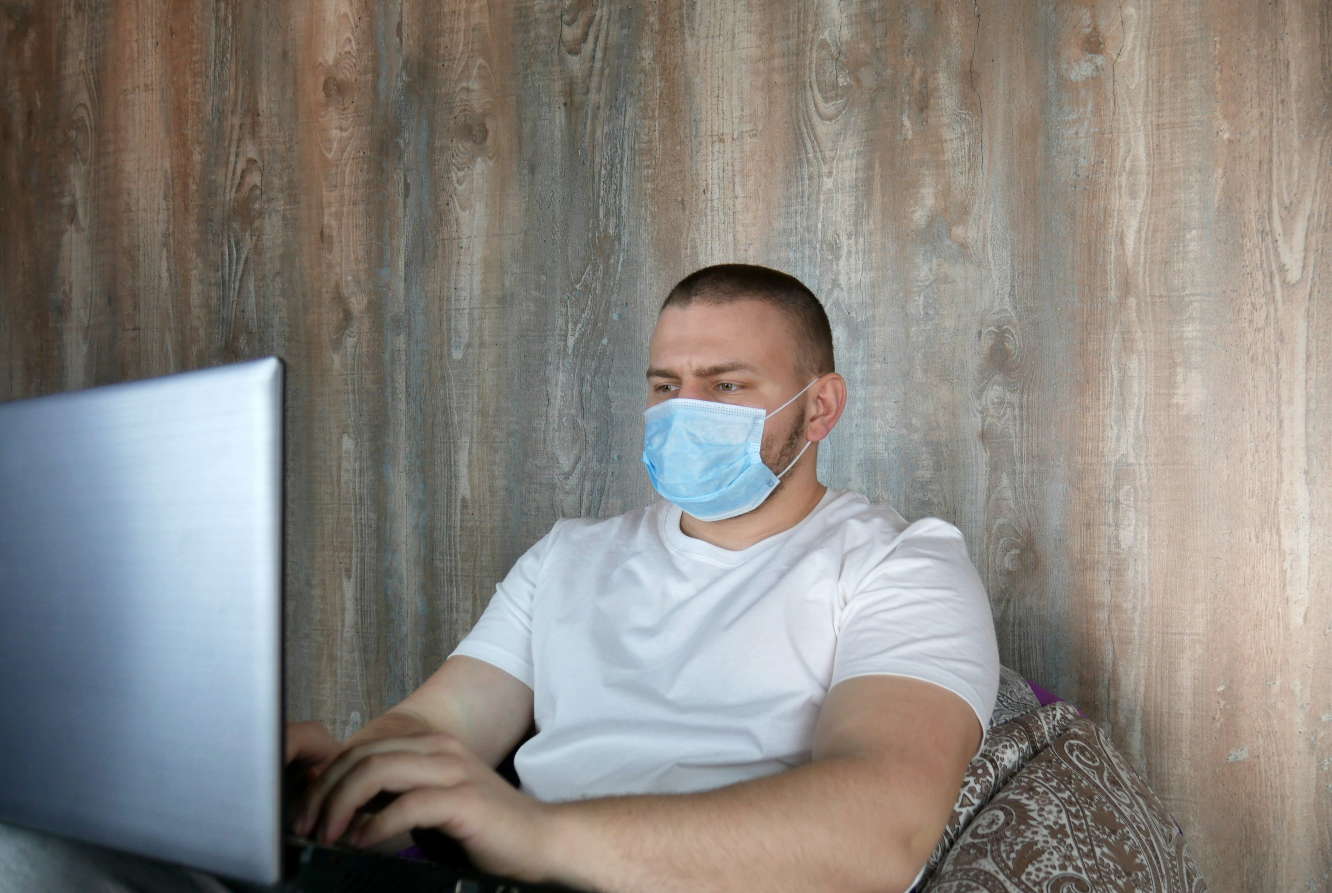 Man in medical mask with a laptop in the house. Coronovirus and home office