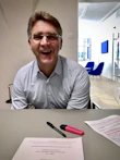 A smiling person attending a live webinar on a tablet, taking notes enthusiastically.