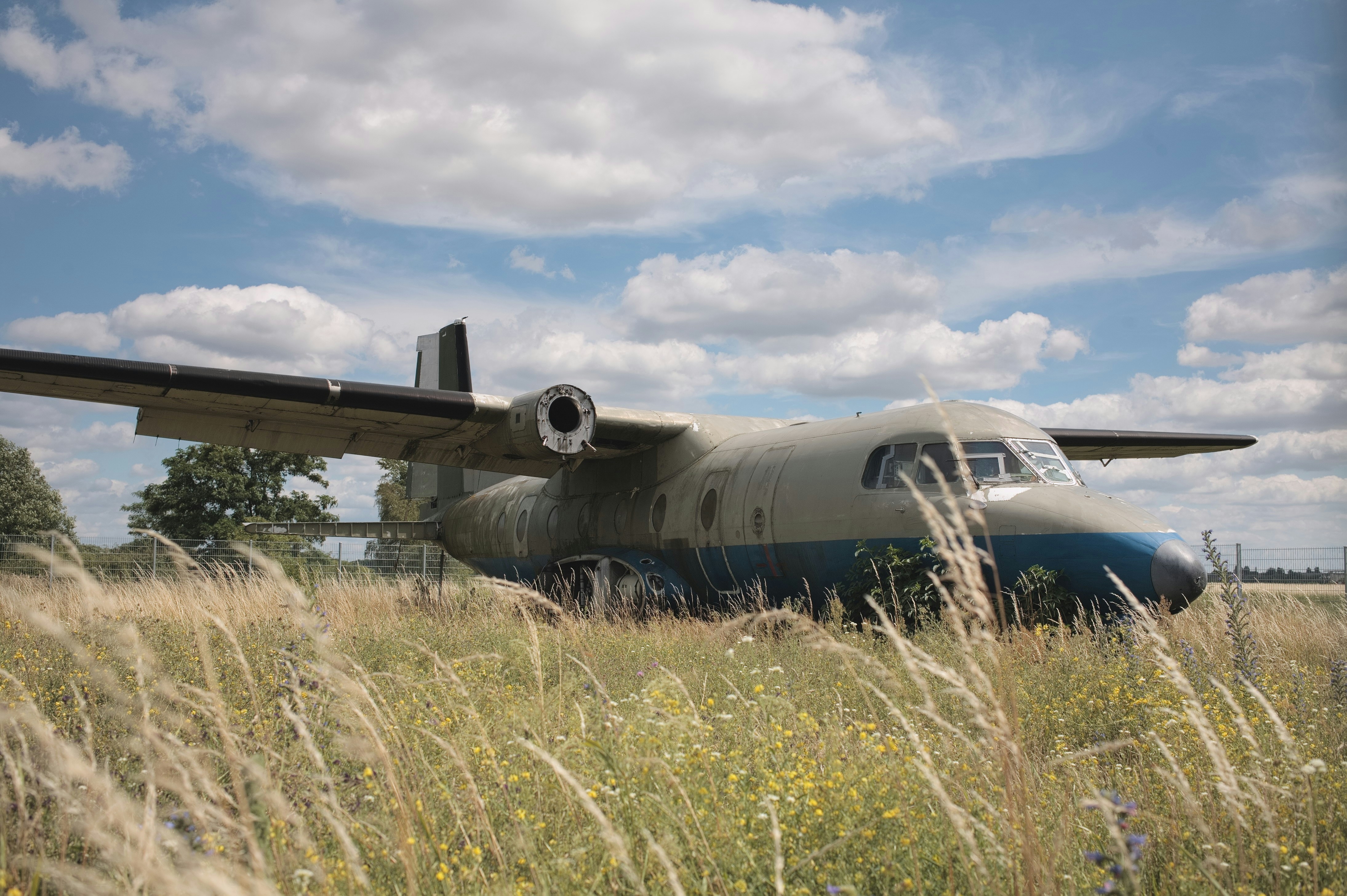 gray airplane on green grass field under white clouds and blue sky during daytime