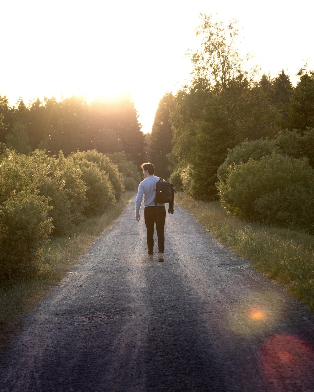 man in black jacket walking on pathway between green grass and trees during daytime