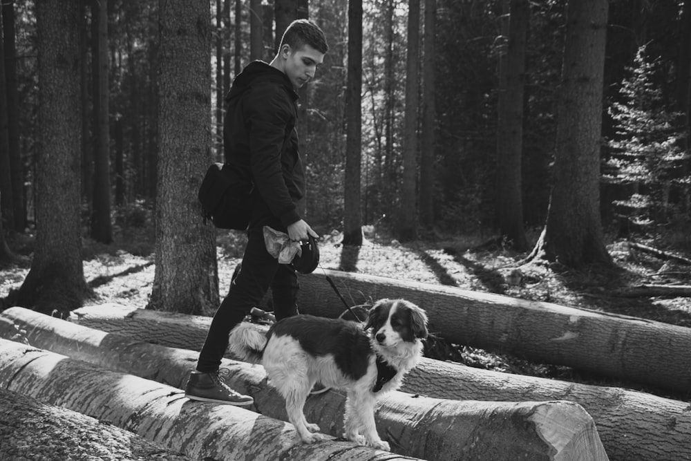 grayscale photo of man in black jacket and pants holding leash of white and brown short