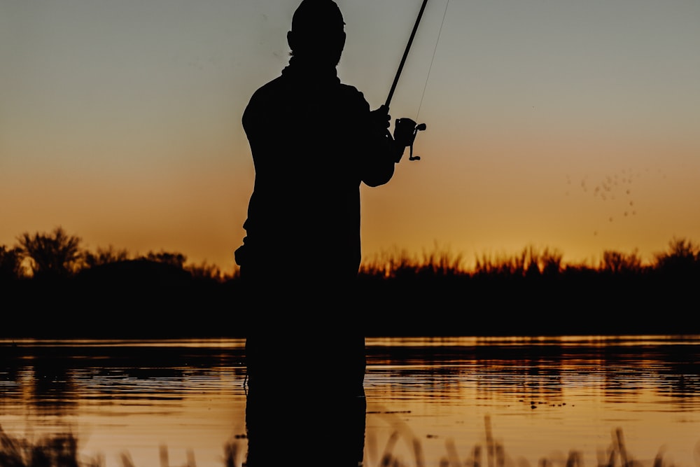 silhouette of man fishing on lake during sunset