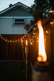 A glowing garden wax torch lighting up a cozy backyard party at dusk.