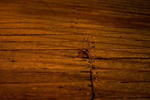 A wooden surface features long, horizontal planks with visible grains and knots. The boards are secured with evenly spaced metal nails, creating a rustic and warm appearance.