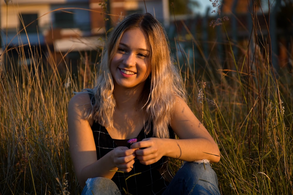 woman in gray tank top and blue denim jeans sitting on green grass during daytime