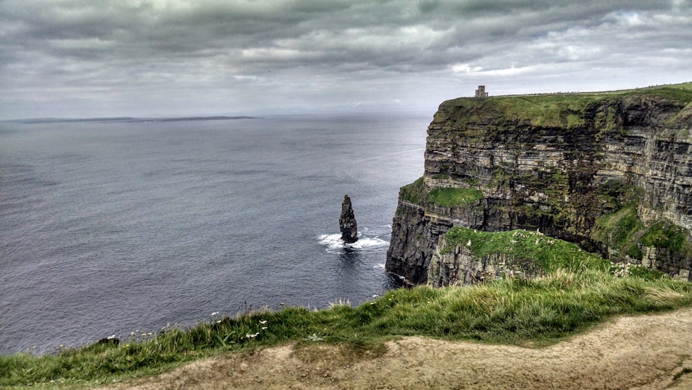 green and brown rock formation beside body of water under cloudy sky during daytime