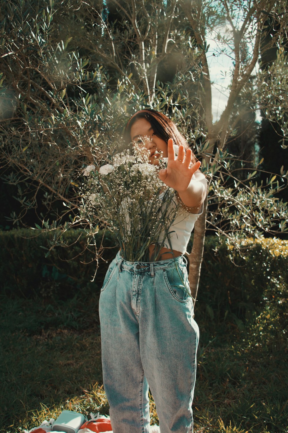 woman in white tank top and blue denim skirt standing near green leaf tree during daytime