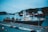 A large ship docked at a harbor with a mountainous backdrop. The ship has industrial equipment and appears to be a fishing or cargo vessel. Another vessel with the name 'OCEANEX' can be seen in the background. The foreground includes a few parked cars and a person walking.