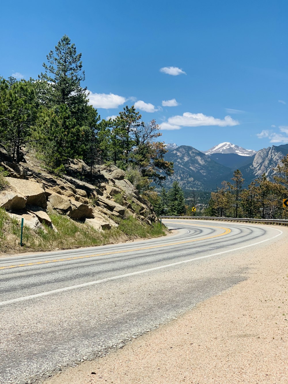 gray asphalt road near green trees and mountain under blue sky during daytime