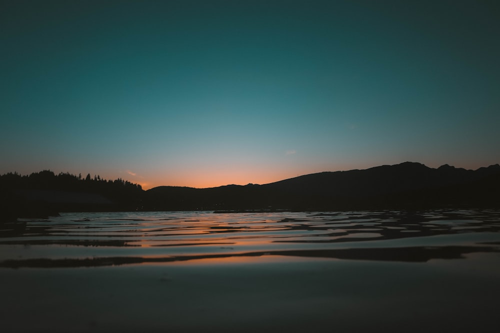 Silueta de la montaña cerca del cuerpo de agua durante la puesta del sol