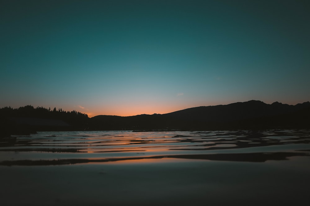 silhouette di montagna vicino allo specchio d'acqua durante il tramonto