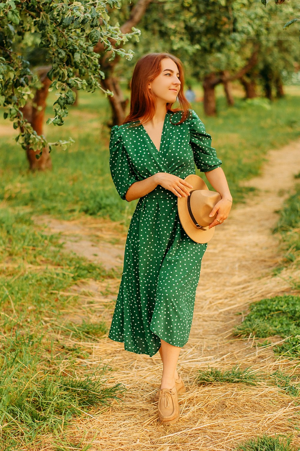 woman in green and black dress holding brown hat standing on brown grass field during daytime