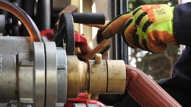 Technician repairing a complex hydraulic system with bright orange safety gear on.