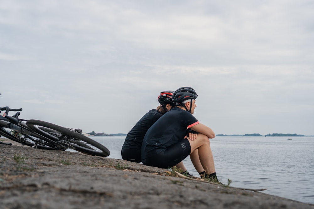 woman in black tank top and black pants sitting on brown rock near body of water