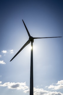 A large wind turbine stands against a clear blue sky, with sunlight peeking through the blades.