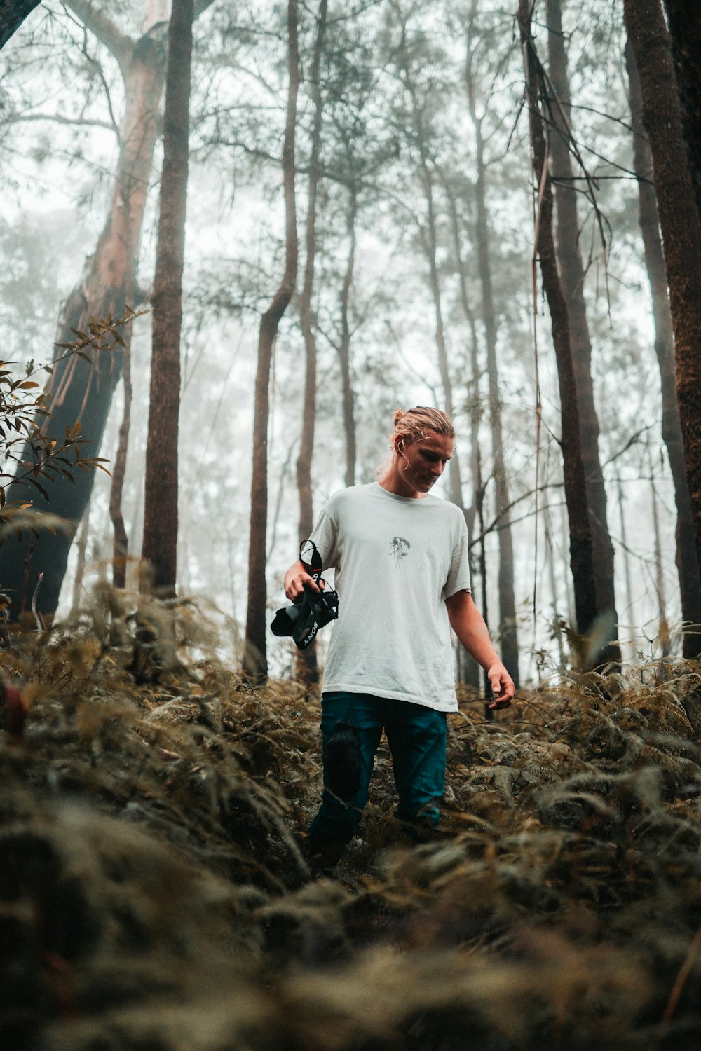 man in gray crew neck t-shirt and blue denim jeans standing on brown dried leaves