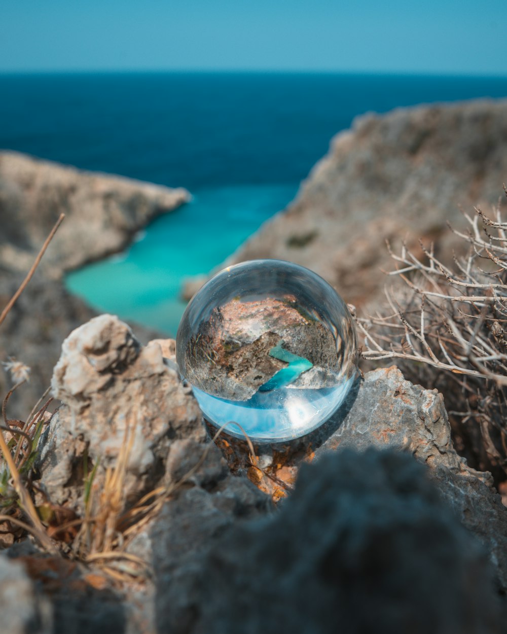 clear glass ball on brown rock near body of water during daytime