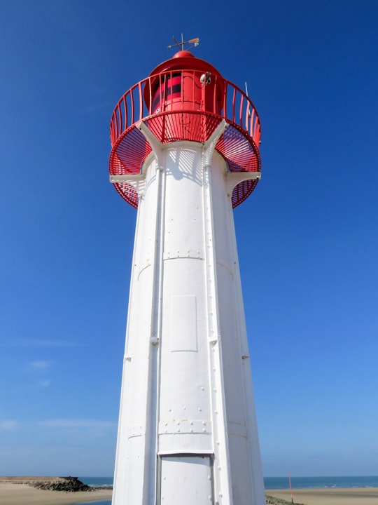 white and red lighthouse under blue sky during daytime in Trouville-sur-Mer France