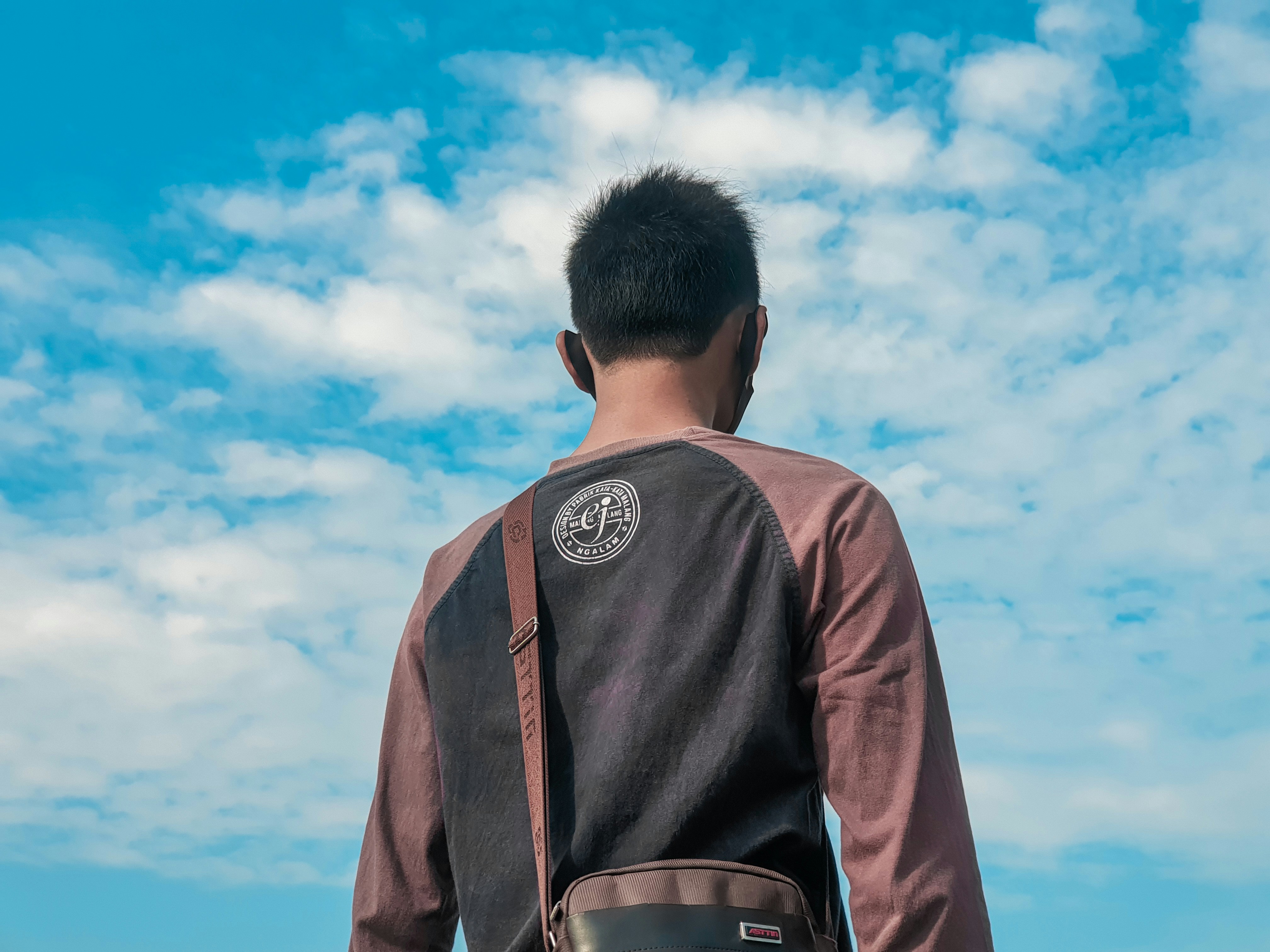 Pria berjaket coklat berdiri di bawah langit biru di siang hari