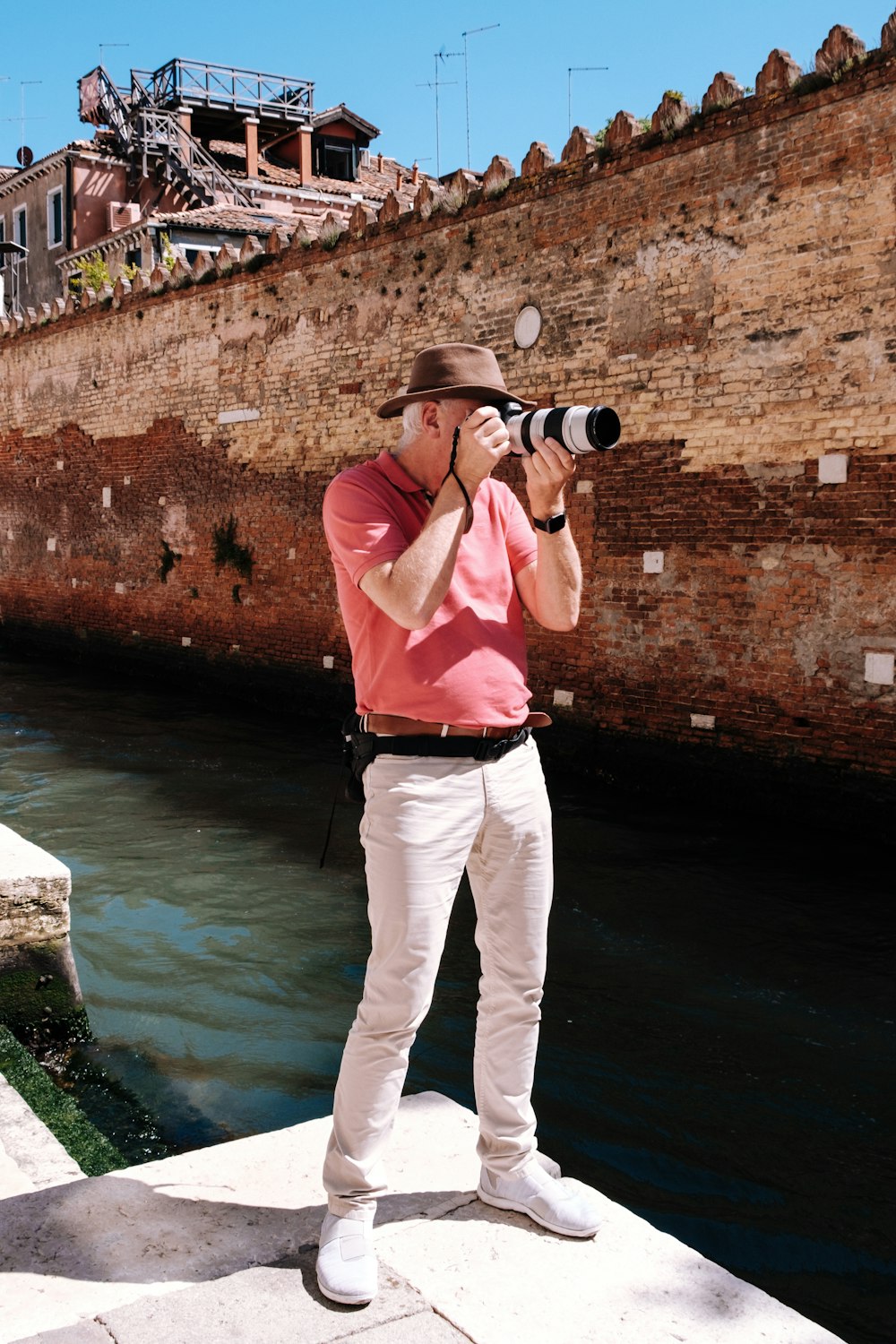 man in pink polo shirt and white pants standing beside brown brick wall