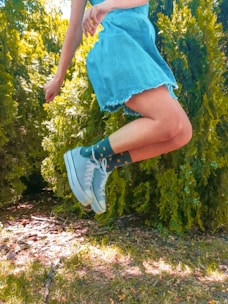 person in blue skirt and white sneakers standing on green grass field during daytime